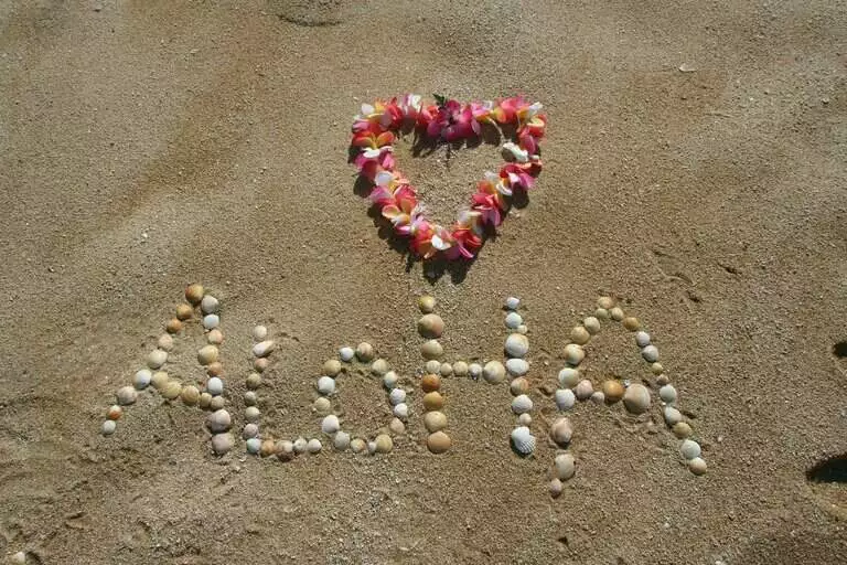 Na pískové pláži kamínky napsáno "Aloha" a květinové srdce